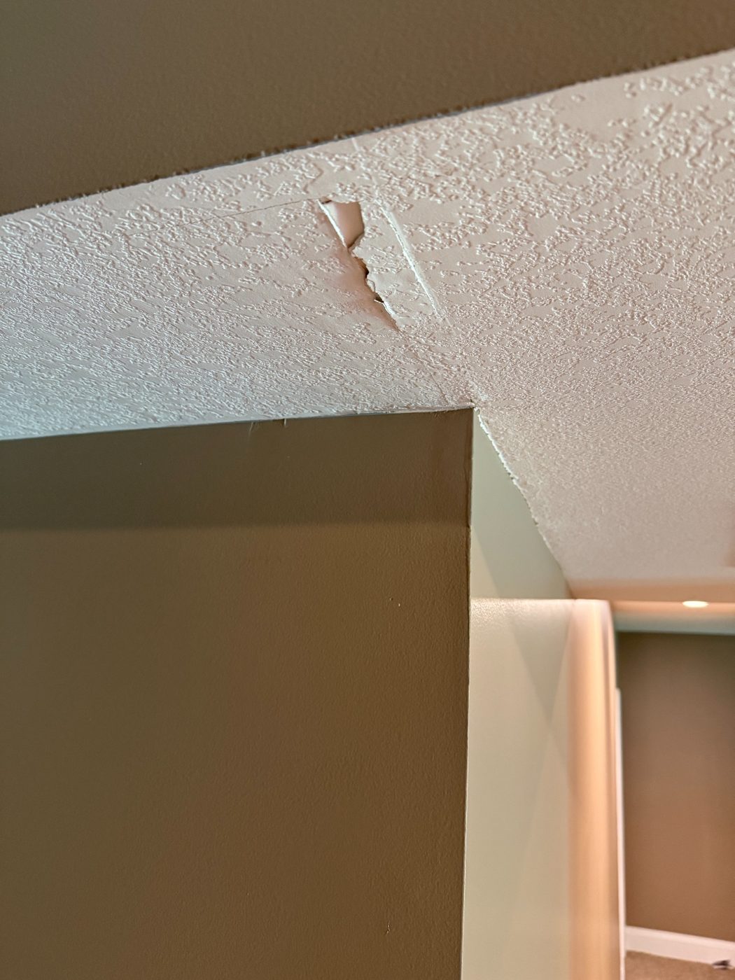 Cracked textured ceiling at a wall corner before repair